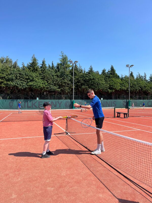 Youth volunteer playing tennis with child.